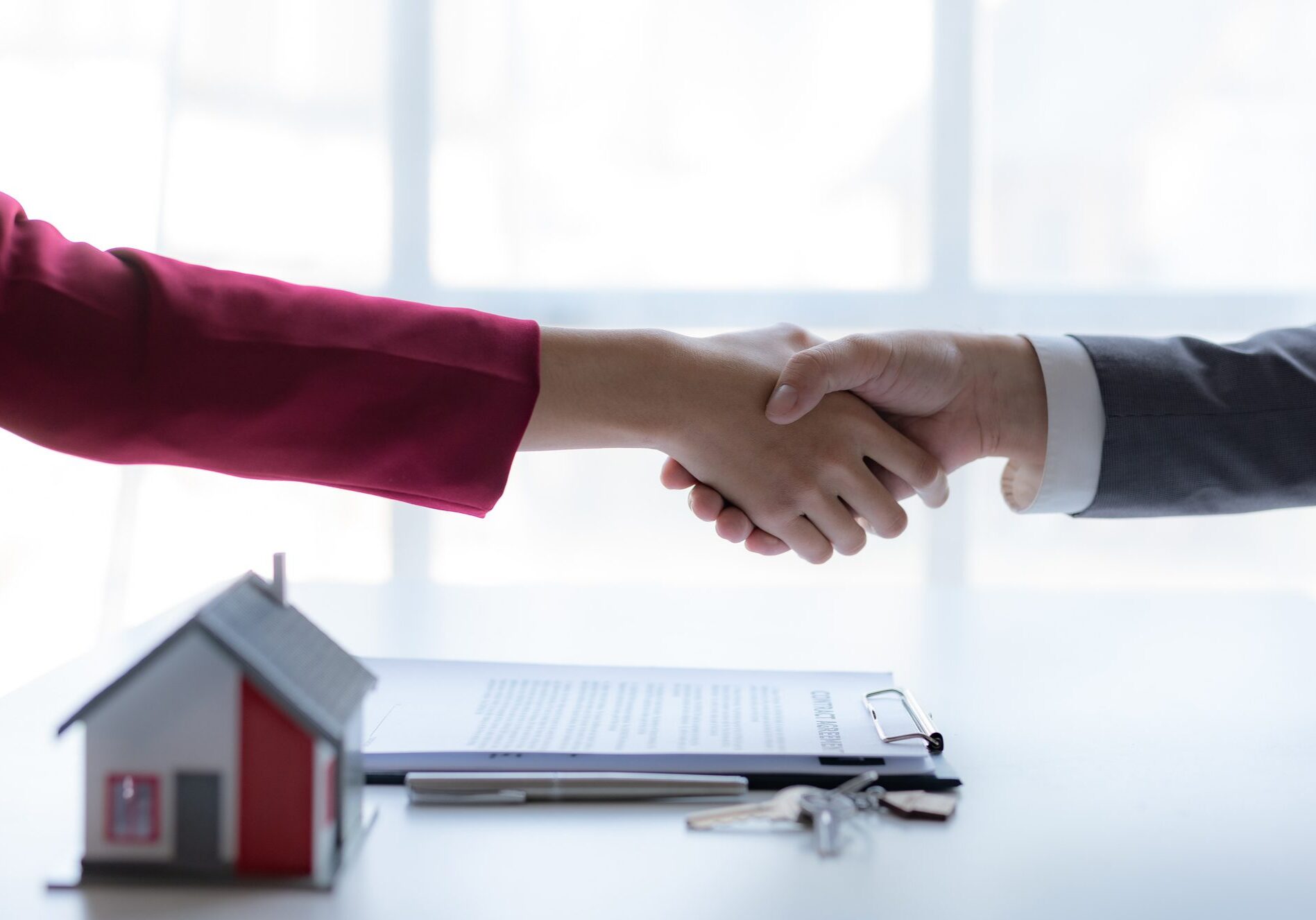 Real estate agent shaking hands with a client to sign a home purchase contract and congratulate the client.